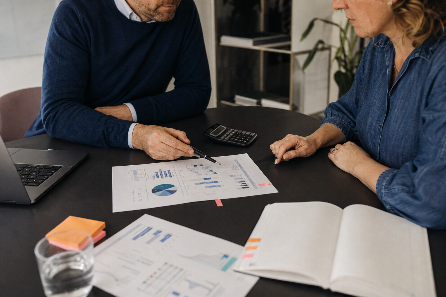 Twee ondernemers bespreken een budget met overzichten, rekenmachine en laptop